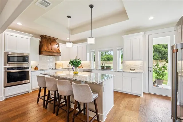 a kitchen with stainless steel appliances granite countertop a stove top oven a sink a microwave a dining table and chairs with wooden floor