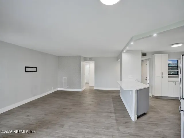 a view of an empty room with wooden floor and kitchen