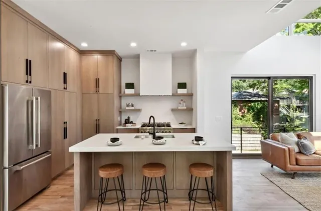 a kitchen with stainless steel appliances a stove a sink a refrigerator white cabinets and couches with wooden floor