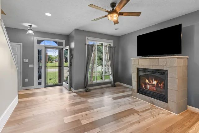 a view of a livingroom with a fireplace a ceiling fan and windows