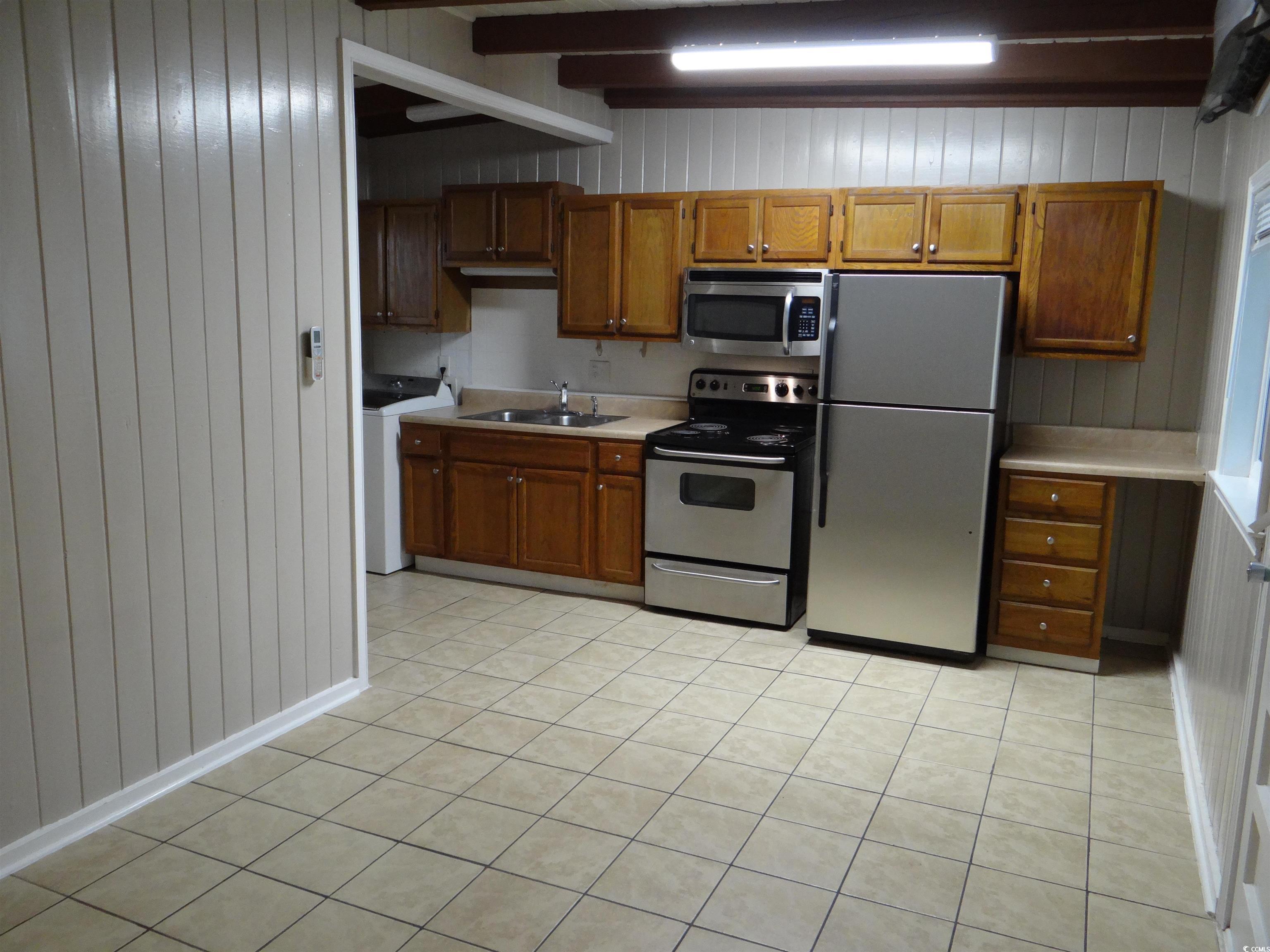3402 Turner Street North Myrtle Beach, SC 29582 - Photo 17 of 26 Kitchen with wood walls, appliances with stainless steel finishes, light countertops, light tile patterned floors, and brown cabinetry