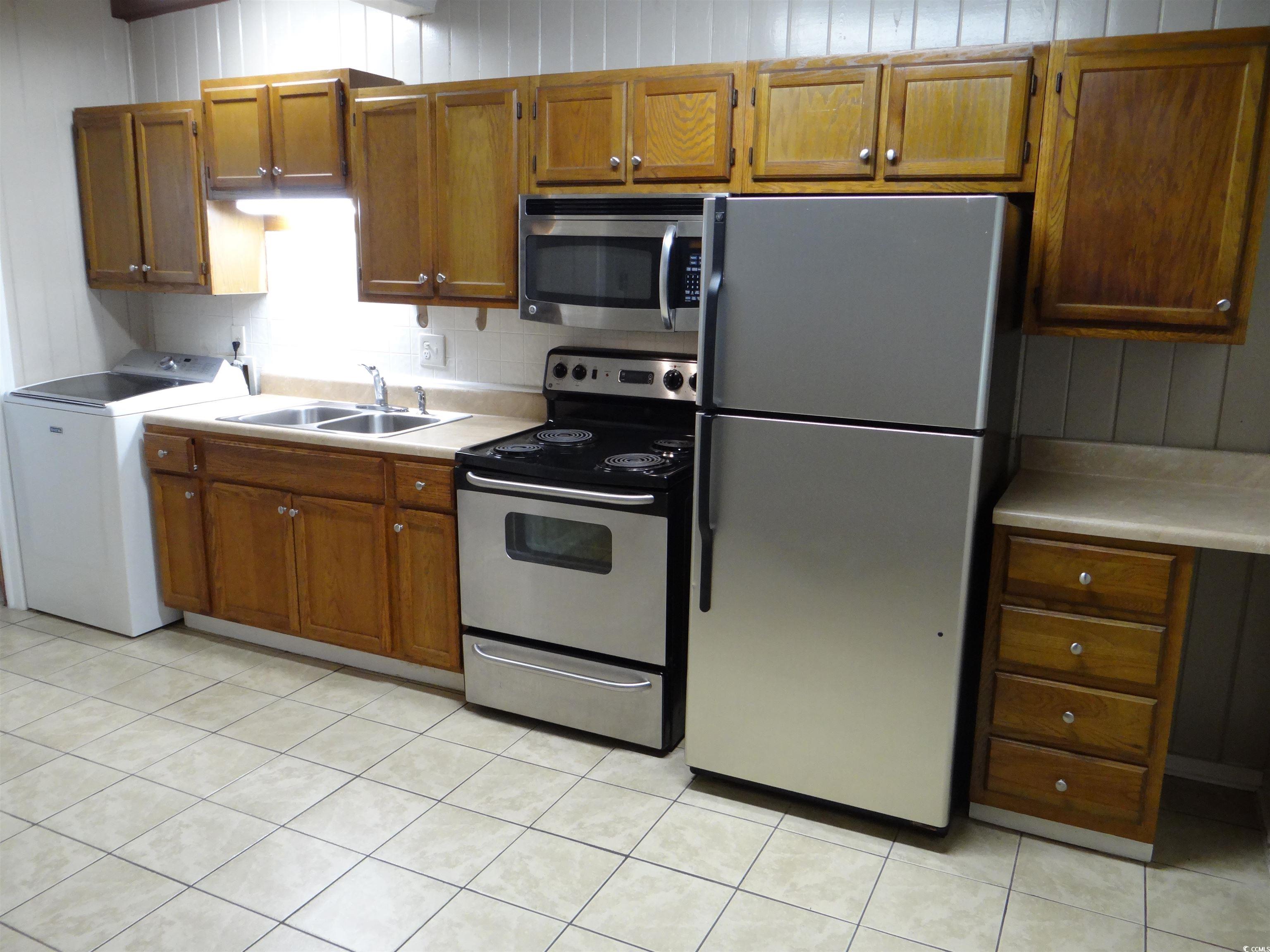 3402 Turner Street North Myrtle Beach, SC 29582 - Photo 19 of 26 Kitchen with stainless steel appliances, washer / dryer, brown cabinetry, light tile patterned floors, and wood walls