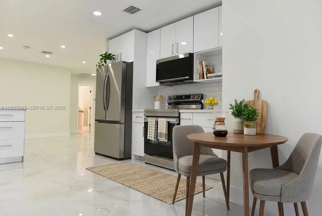 a kitchen with stainless steel appliances a dining table chairs refrigerator and microwave