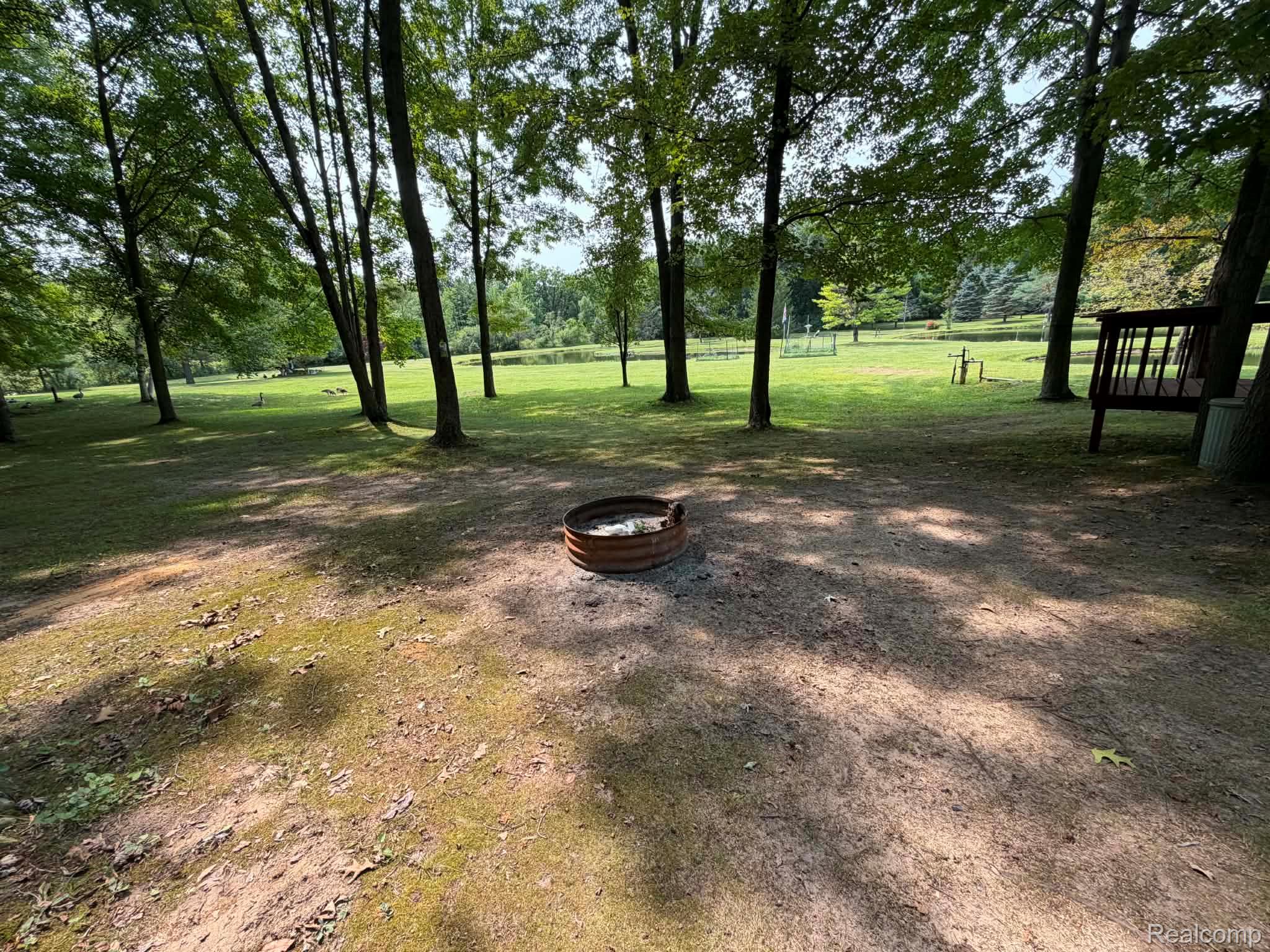 8110 North Latson Road Howell, MI 48855 - Photo 42 of 48 Spacious grounds featuring mature shade trees, open lawn area, and a fire pit ring—ideal for outdoor gatherings and recreation