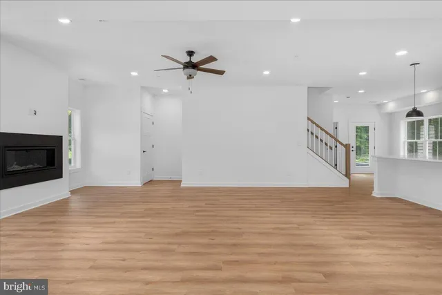 a view of an empty room with wooden floor and a kitchen