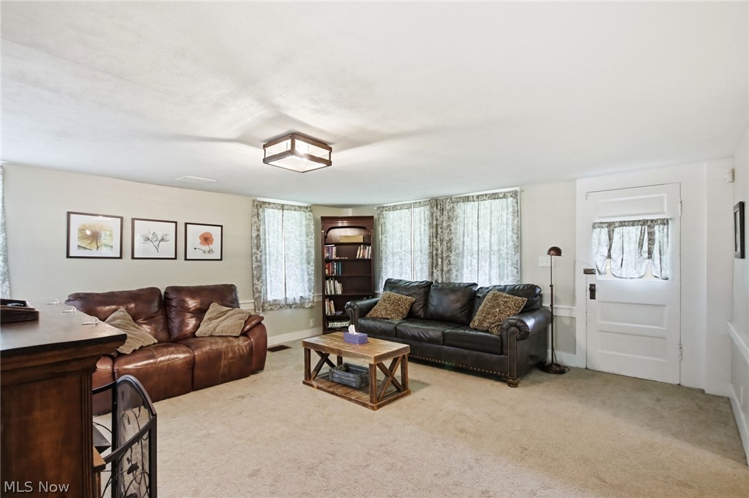 Spacious living area featuring neutral carpeting, light-colored walls, and multiple windows with patterned curtains