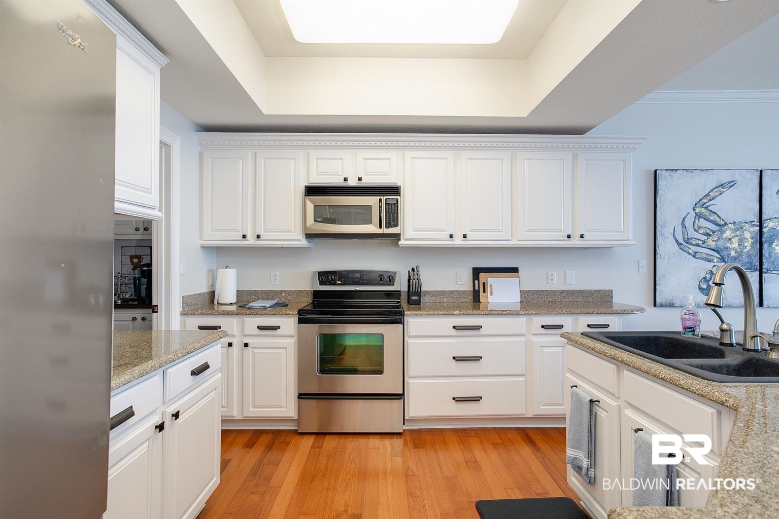 27800 Canal Road, Unit 411 Orange Beach, AL 36561 - Photo 7 of 49 Kitchen featuring hardwood flooring, white cabinetry with black hardware, stainless steel appliances, granite countertops, and a built-in sink