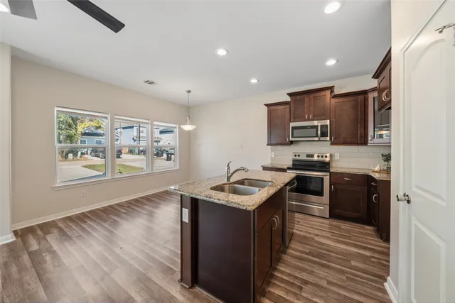 a kitchen with stainless steel appliances granite countertop a stove top oven a sink dishwasher a refrigerator and a microwave oven with wooden floor