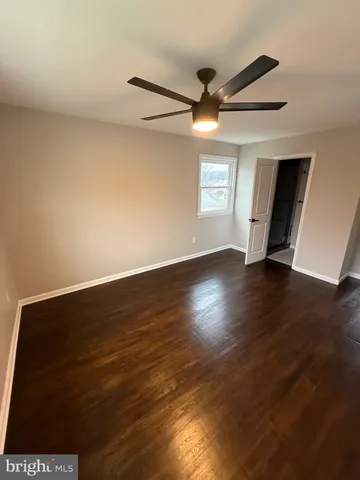 a view of an empty room with wooden floor and a ceiling fan