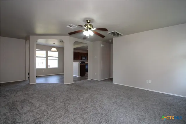 an empty room with chandelier fan and windows