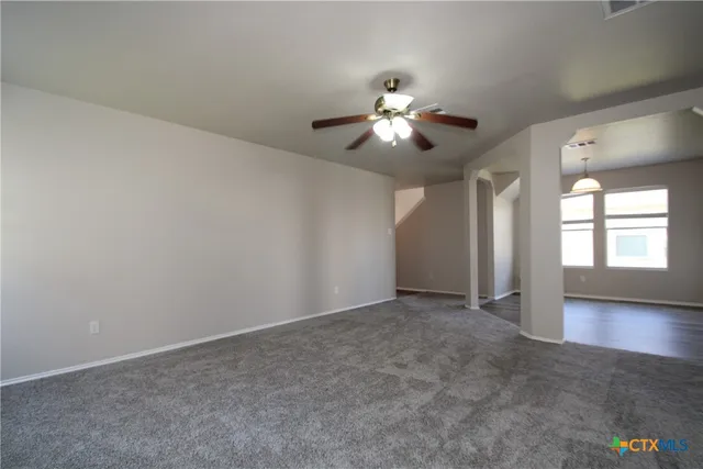 an empty room with chandelier fan and windows