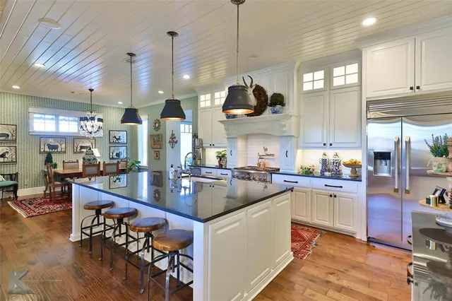 a kitchen with stainless steel appliances granite countertop a stove top oven a sink a dining table and chairs with wooden floor