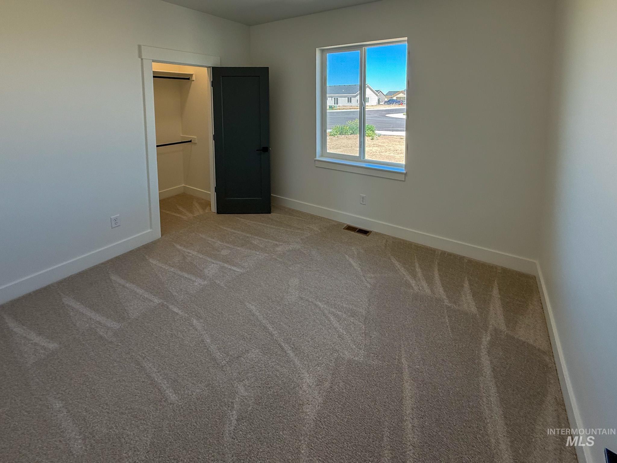 1419 Cardon Court Rupert, ID 83350 - Photo 11 of 15 Carpeted room featuring a double-hung window, a walk-in closet with built-in shelving and hanging rods, and a dark paneled door with matte black hardware