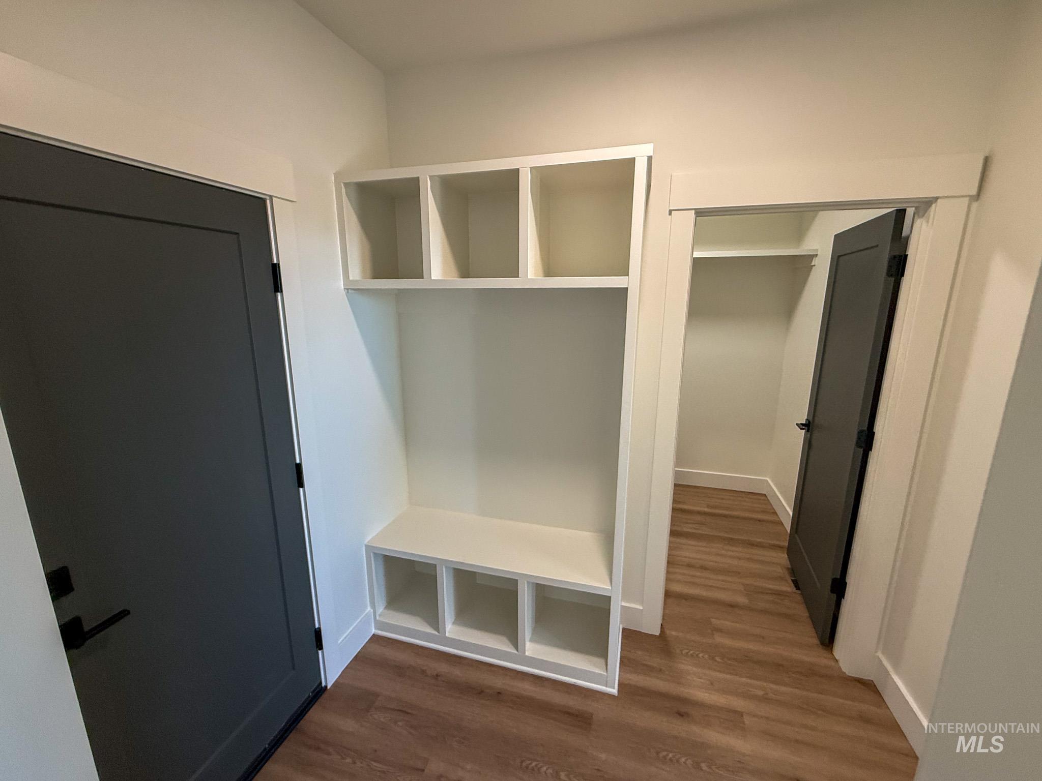 1419 Cardon Court Rupert, ID 83350 - Photo 6 of 15 Entryway featuring built-in white cabinetry with open shelving and bench seating, wood-finish flooring, and dark-paneled doors with matte black hardware