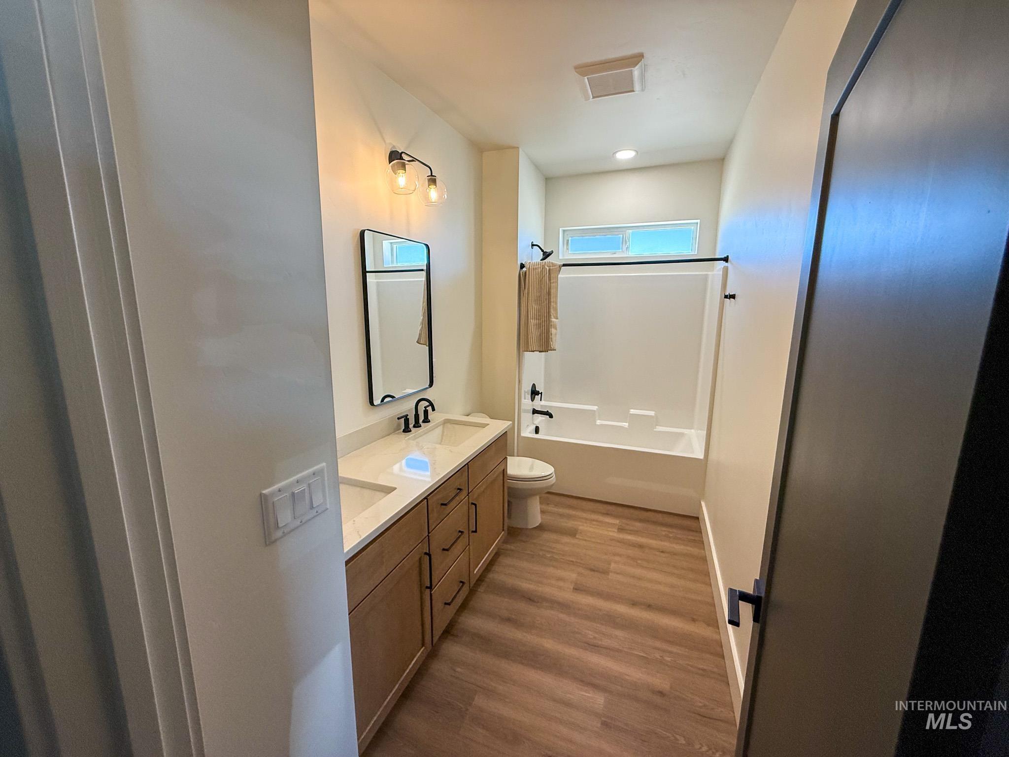 1419 Cardon Court Rupert, ID 83350 - Photo 10 of 15 Bathroom featuring a dual vanity with light-colored countertops, wood-finish flooring, and a white bathtub with a window above