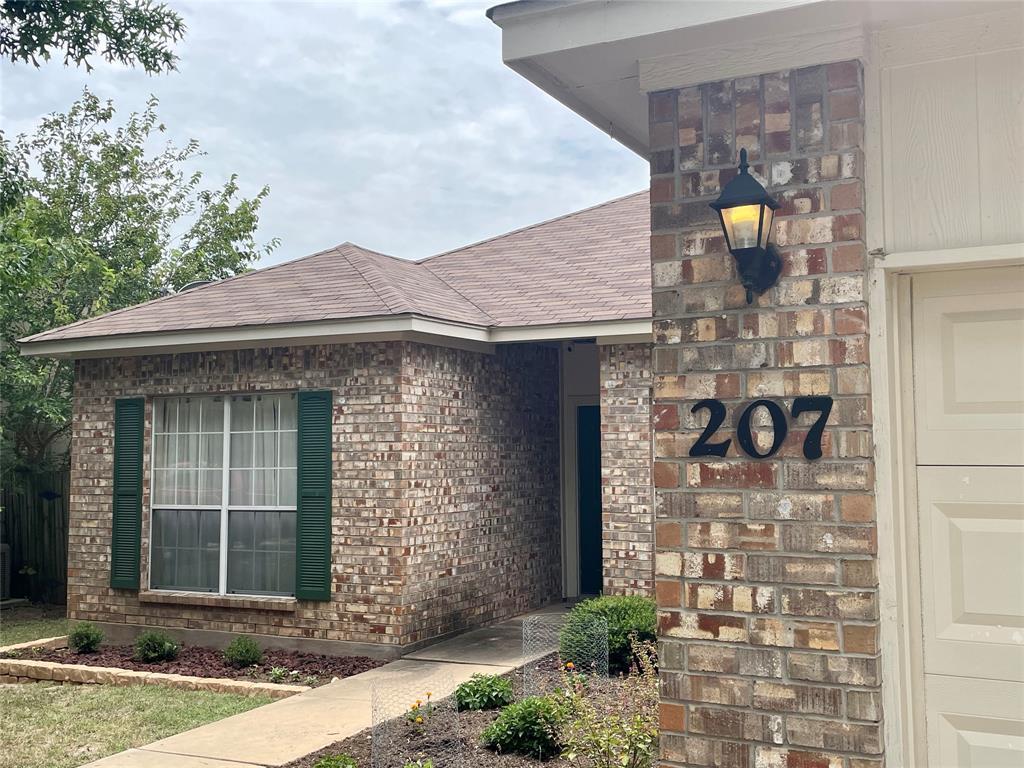 207 Kates Way Hutto, TX 78634 - Photo 2 of 24 Brick exterior featuring dark green shutters, a concrete walkway, and landscaped garden beds