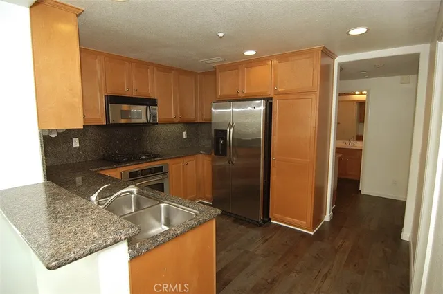 a kitchen with stainless steel appliances granite countertop a refrigerator a stove and a sink with wooden floor