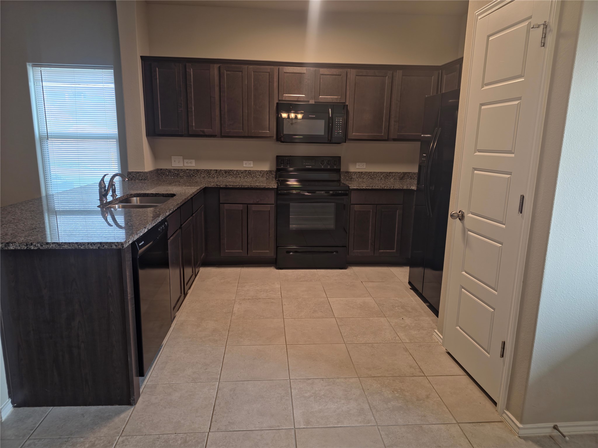 140 Dodge Road Georgetown, TX 78626 - Photo 5 of 14 Kitchen featuring dark wood-finish cabinetry, granite-style countertops, black appliances, a double basin stainless steel sink with gooseneck faucet, and light-colored tile flooring