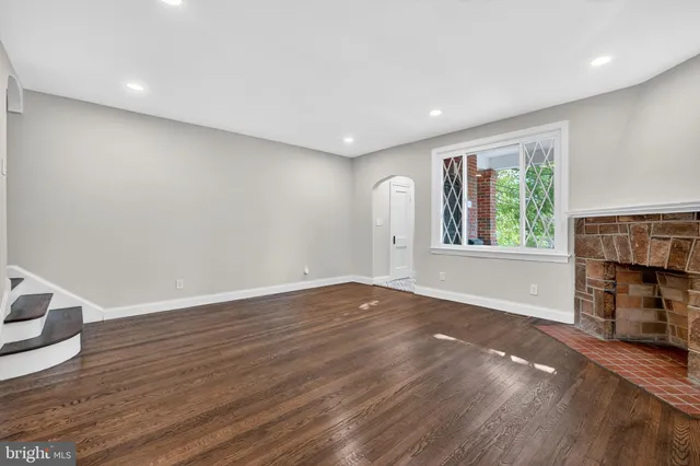a view of an empty room with wooden floor fireplace and a window