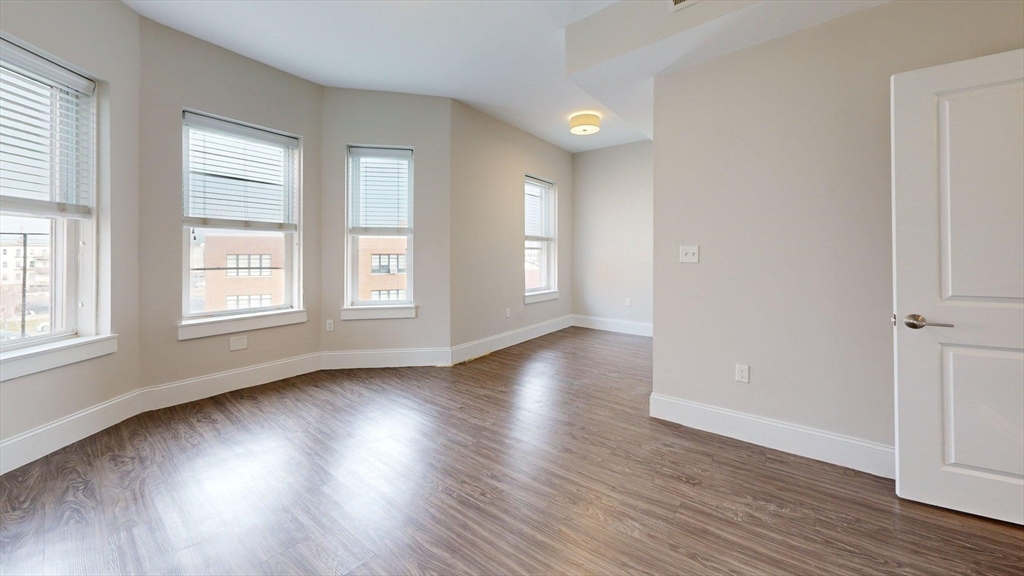 133 Paris Street, Unit 2 Boston, MA 02128 - Photo 21 of 26 an empty room with wooden floor and windows with curtains view
