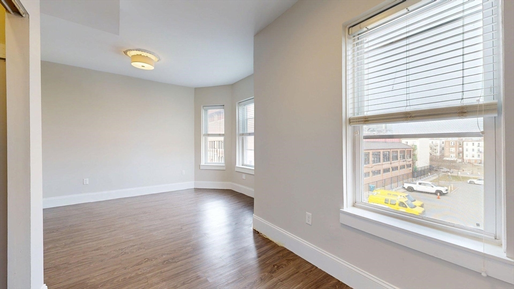 133 Paris Street, Unit 2 Boston, MA 02128 - Photo 7 of 26 a view of an empty room with a window and wooden floor