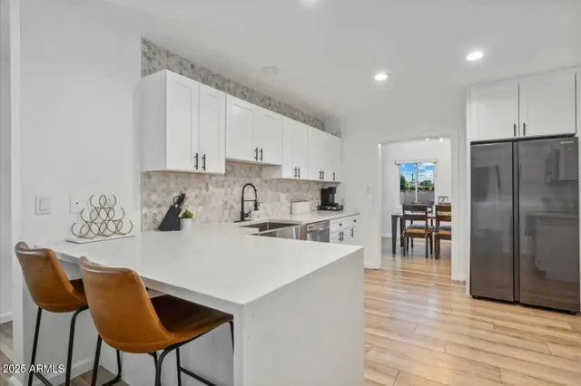 a kitchen with stainless steel appliances granite countertop a stove a sink a refrigerator and white cabinets with wooden floor