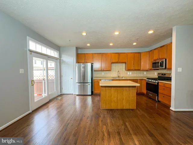 a kitchen with stainless steel appliances granite countertop wooden cabinets a refrigerator a sink a stove and a wooden floors