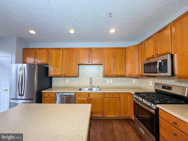 a kitchen with stainless steel appliances granite countertop a stove top oven a refrigerator a sink and dishwasher with wooden floor