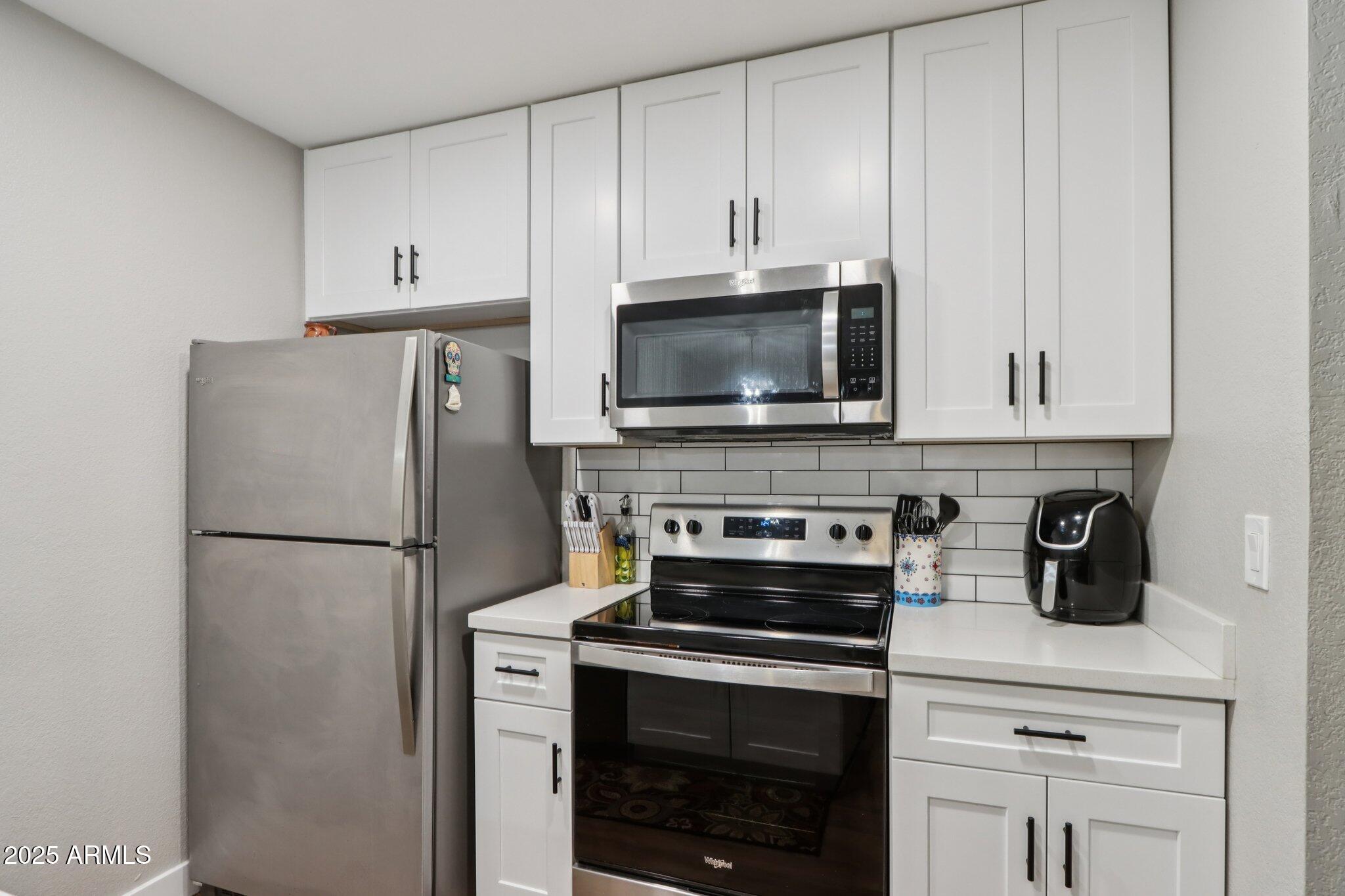 510 North Alma School Road, Unit 174 Mesa, AZ 85201 - Photo 14 of 38 a white kitchen with stainless steel appliances a stove a microwave and a refrigerator