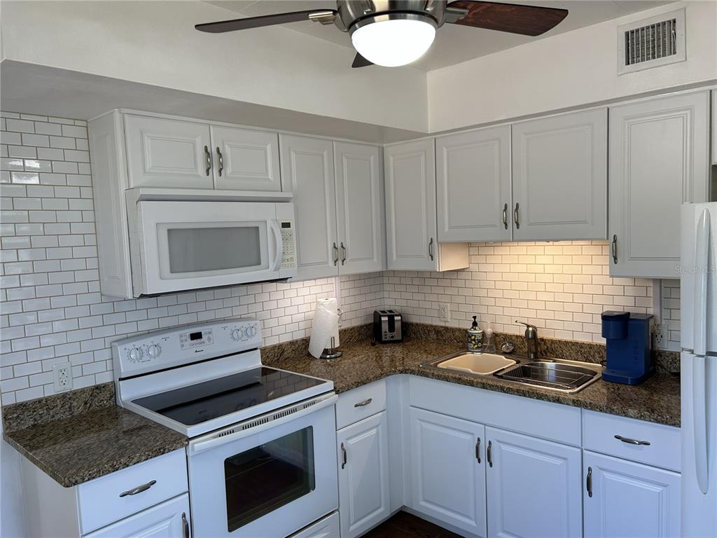4154 57th Street North, Unit 274 Kenneth City, FL 33709 - Photo 7 of 28 a kitchen with white cabinets a sink dishwasher and a stove with wooden floor
