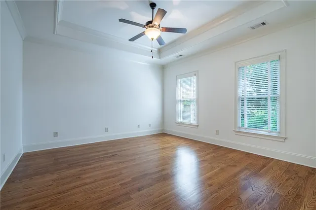 an empty room with wooden floor chandelier fan and windows
