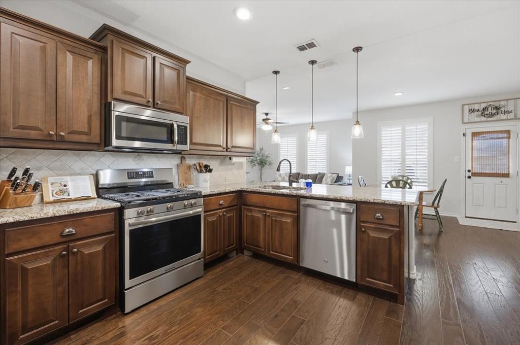 a kitchen with stainless steel appliances granite countertop wooden cabinets a stove a sink and dishwasher with wooden floor