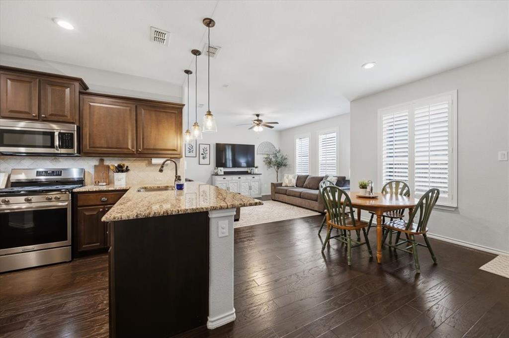 448 Spring Drive Saginaw, TX 76131 - Photo 15 of 40 a kitchen with stainless steel appliances granite countertop a stove a refrigerator a kitchen island a dining table and chairs with wooden floor