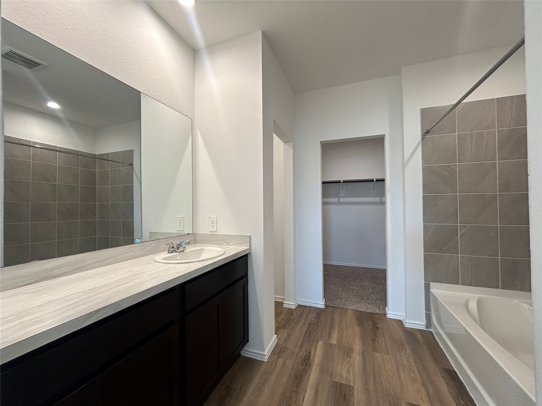 1739 Royal Rim Drive Houston, TX 77014 - Photo 9 of 20 This bathroom features a sleek design with a large mirror, spacious vanity, and modern sink. It includes a tiled shower and a separate bathtub. The room is connected to a walk-in closet, and the flooring is a stylish wood laminate.