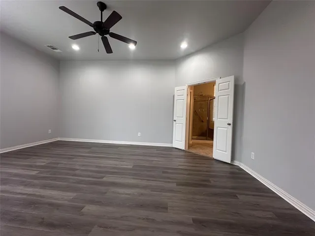 a view of an empty room with wooden floor and a ceiling fan
