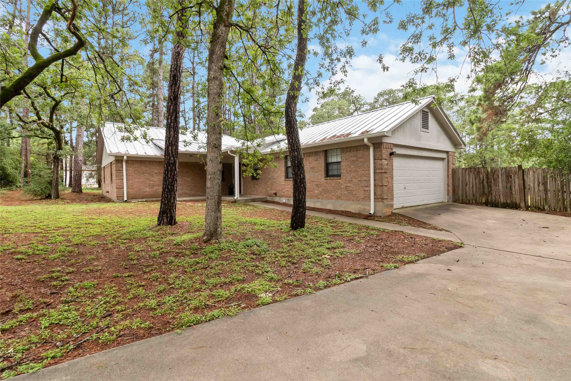 326 Pine View Loop Bastrop, TX 78602 - Photo 2 of 30 A classic brick exterior home sits nestled among mature trees, featuring a concrete driveway and attached garage.