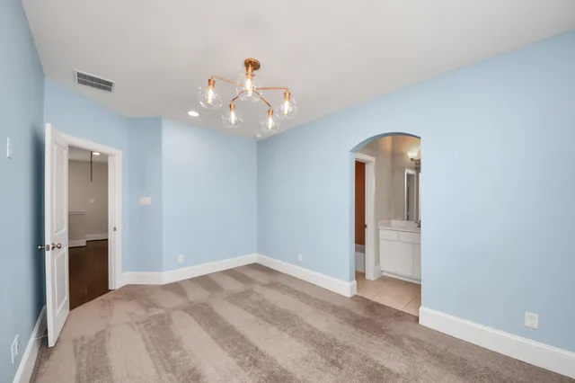 an empty room with chandelier fan and kitchen view