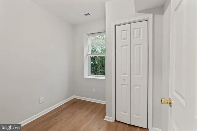 an empty room with wooden floor closet and windows