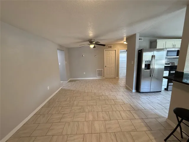 a view of a livingroom with a chandelier fan and refrigerator in a kitchen