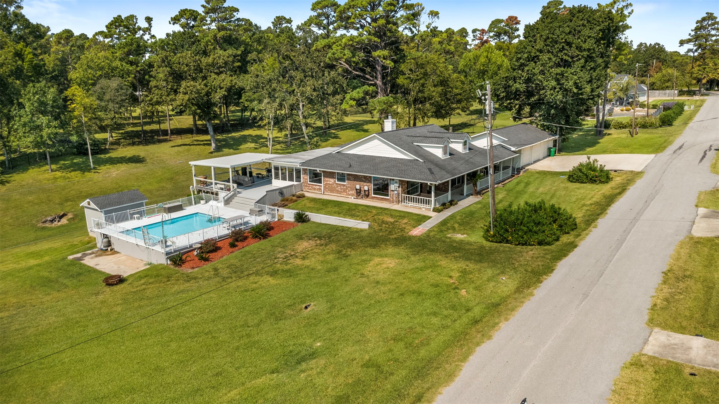 381 West Lake Drive Point Blank, TX 77364 - Photo 27 of 33 This aerial perspective showcases the full beauty of the property — wraparound porch, large pool with decking, and expansive lot in a peaceful lakeside neighborhood.