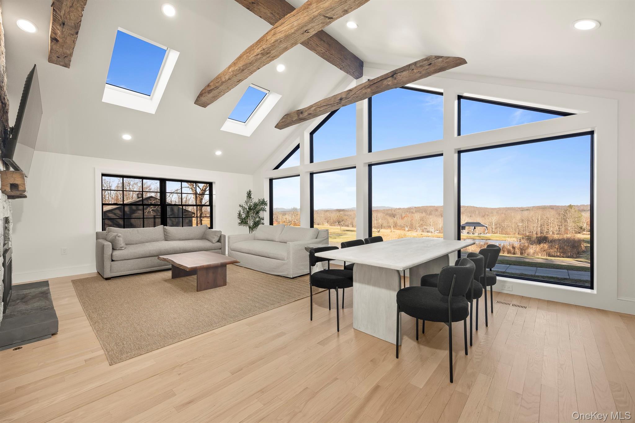 Living area featuring a skylight, light wood flooring, high vaulted ceiling, recessed lighting, and beamed ceiling