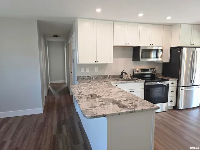 a kitchen with kitchen island granite countertop a stove a sink a refrigerator and white cabinets with wooden floor