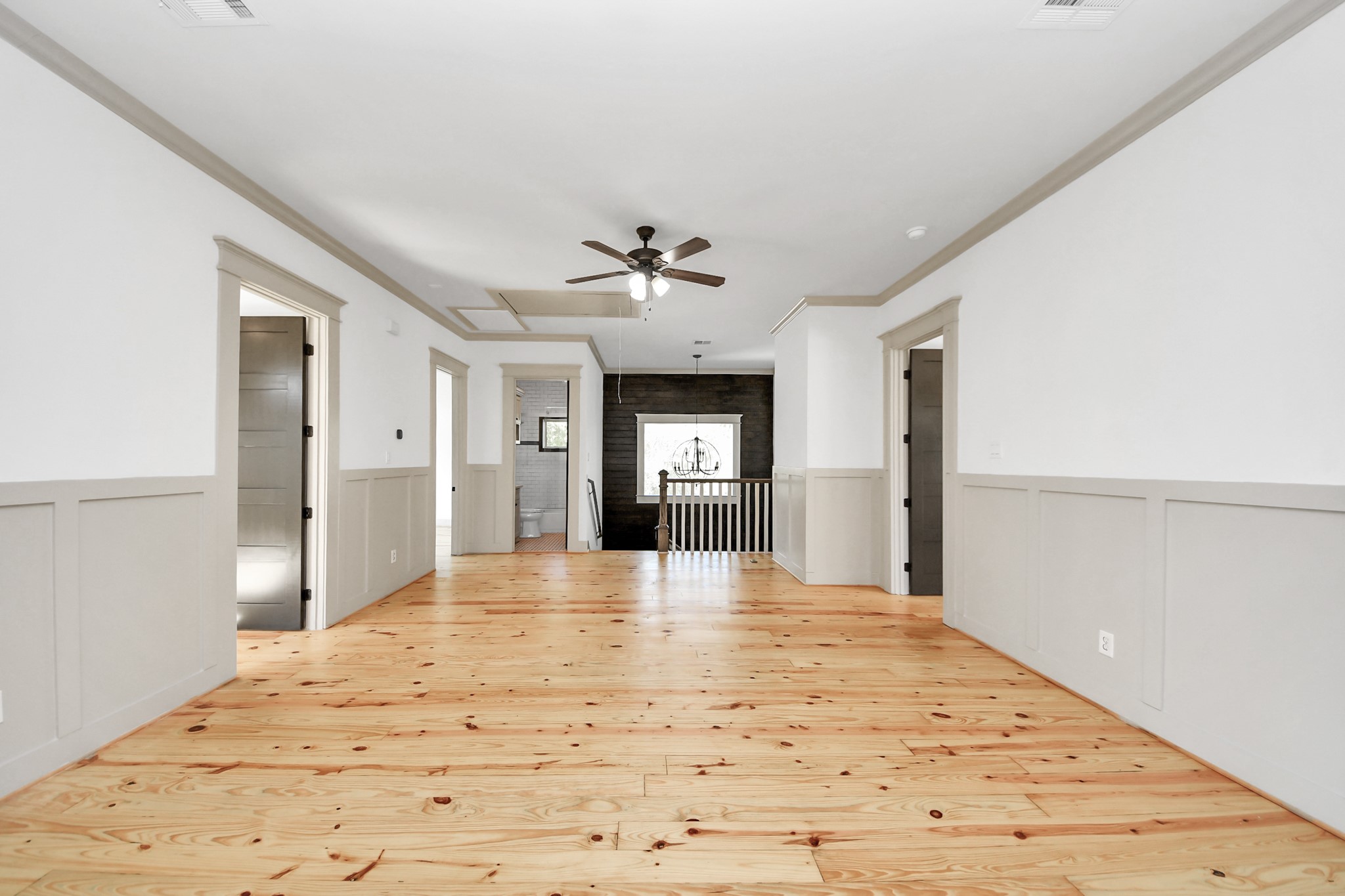 1202 Archer Street Houston, TX 77009 - Photo 33 of 46 This spacious, light-filled room features natural wood flooring, elegant white and gray wainscoted walls, and a ceiling fan. Multiple doorways connect to surrounding spaces, creating an open, inviting, and versatile layout.