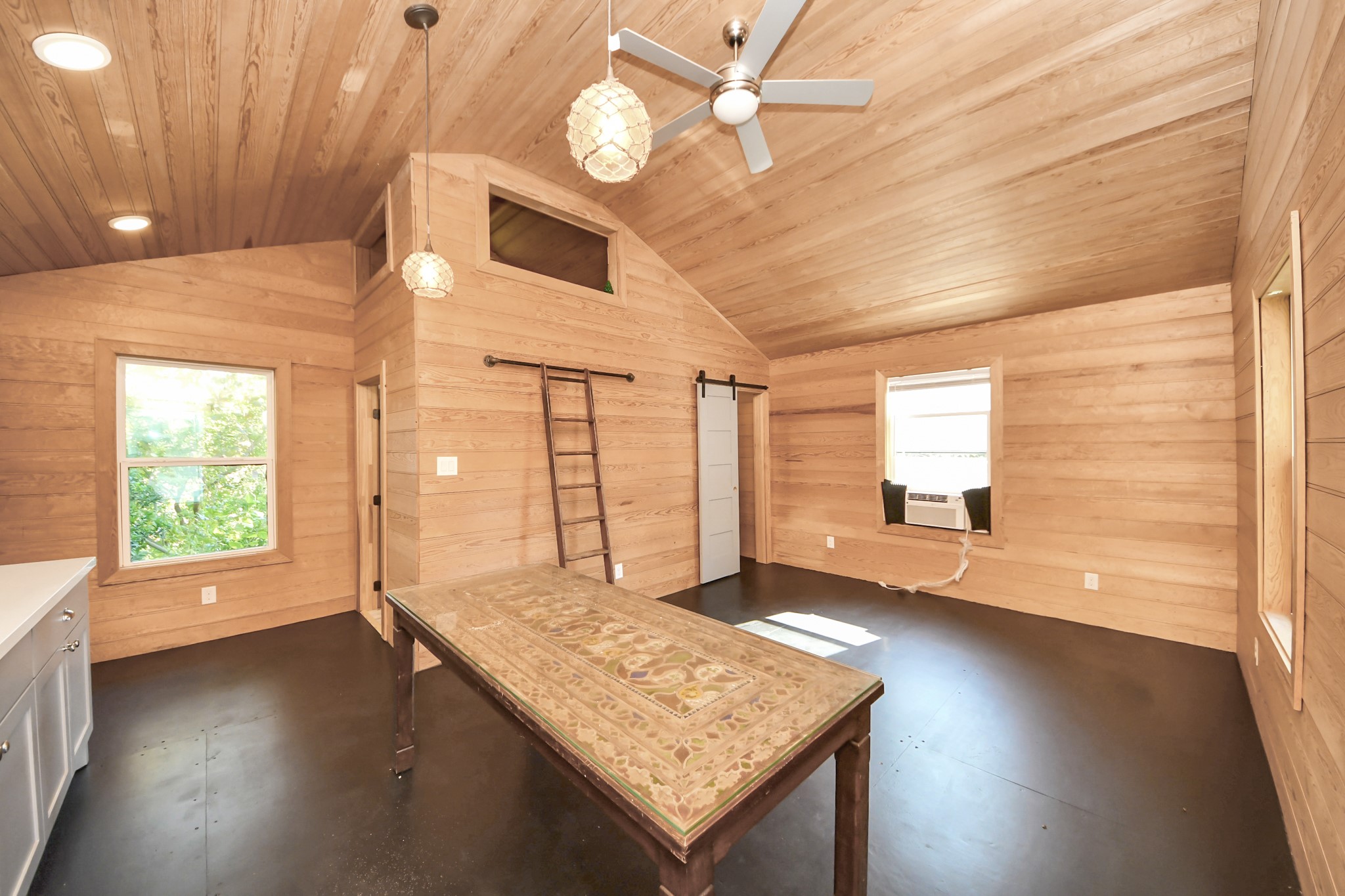 1202 Archer Street Houston, TX 77009 - Photo 37 of 46 This cozy treehouse features warm wood-paneled walls and ceiling, creating a cabin-like atmosphere. It includes a comfortable bed, a rustic wooden table, and ample natural light from two windows. The space offers a charming, inviting ambiance.