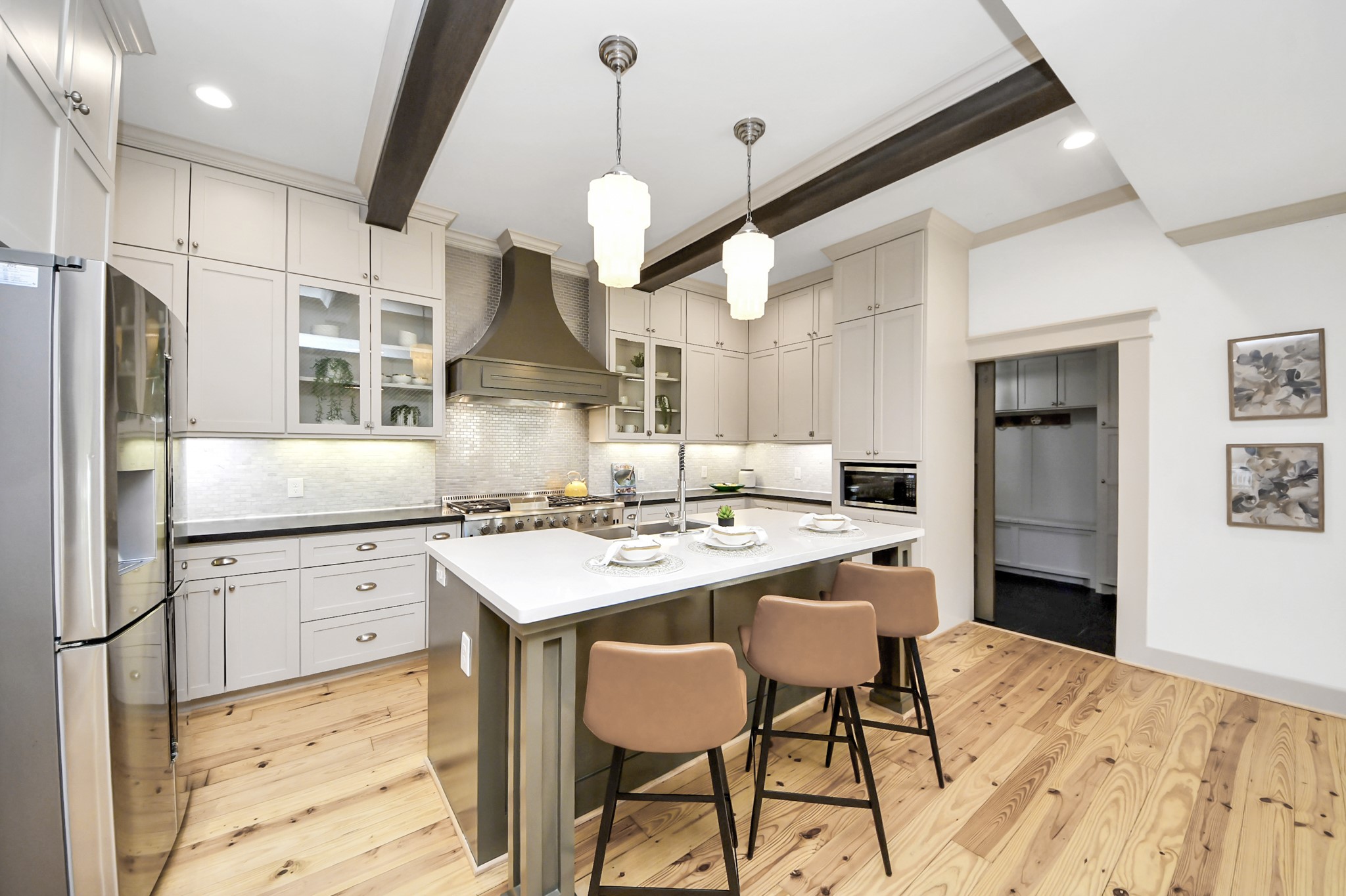 1202 Archer Street Houston, TX 77009 - Photo 10 of 46 Handcrafted kitchen features sleek white cabinetry, a large stone island with a sink and seating, stainless steel appliances, and elegant pendant lighting. The space is accented by a stylish range hood and dark hardwood flooring.