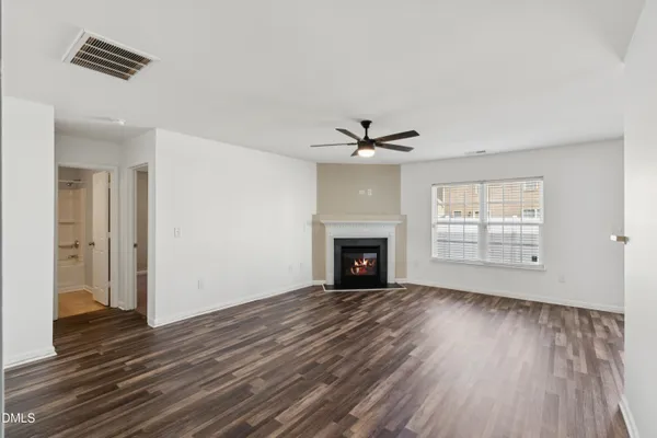 a view of an empty room with wooden floor fireplace and a window