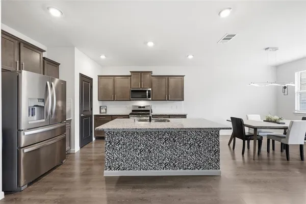 a kitchen with stainless steel appliances granite countertop a stove top oven a sink a dining table and chairs