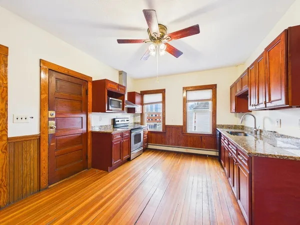 a kitchen with stainless steel appliances granite countertop a stove top oven a chimney cabinets and wooden floor