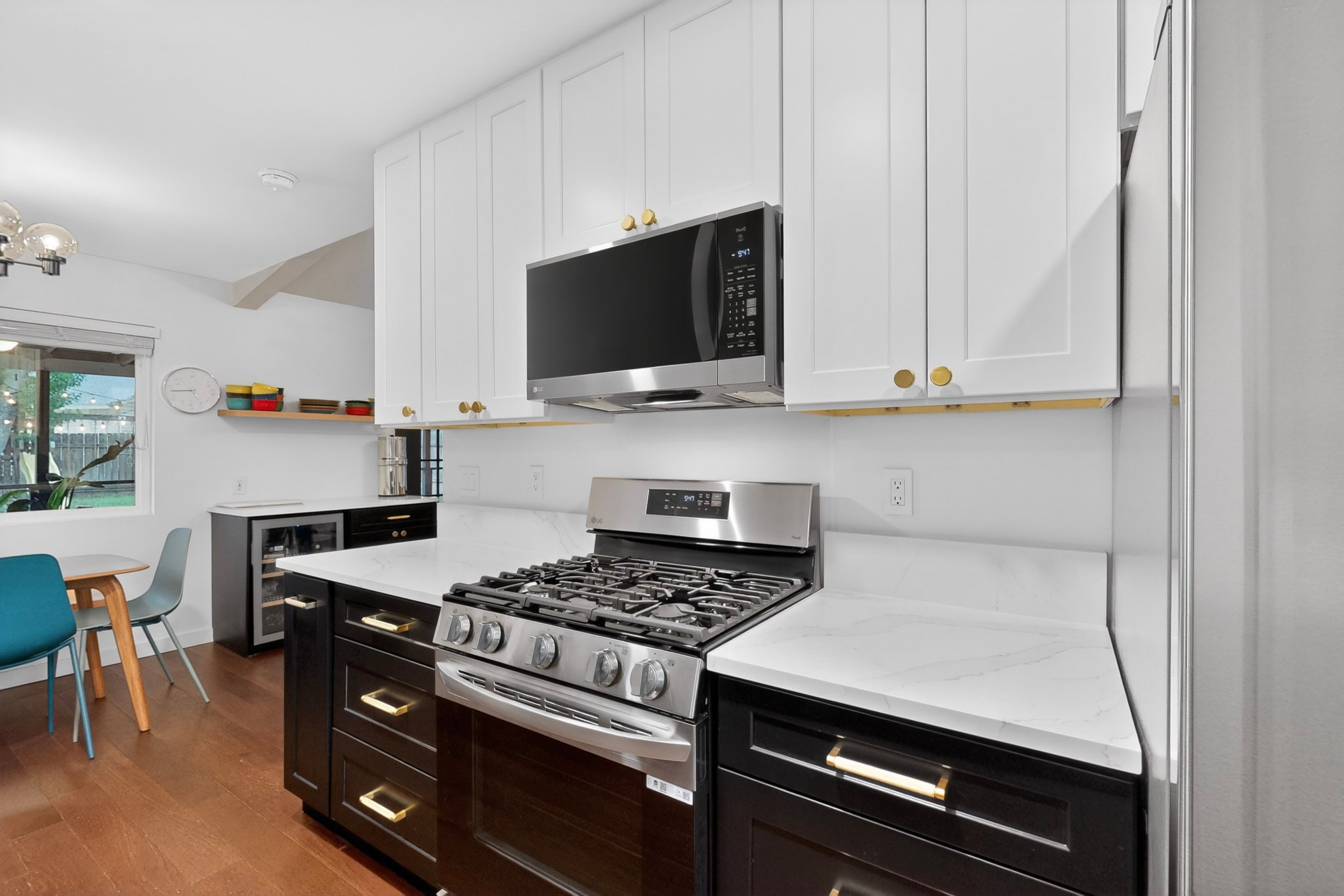5541 Pine Place Austin, TX 78744 - Photo 13 of 33 Modern kitchen featuring white upper cabinetry, dark lower cabinetry with gold-toned hardware, white solid surface countertops, a stainless steel gas range, and a built-in microwave