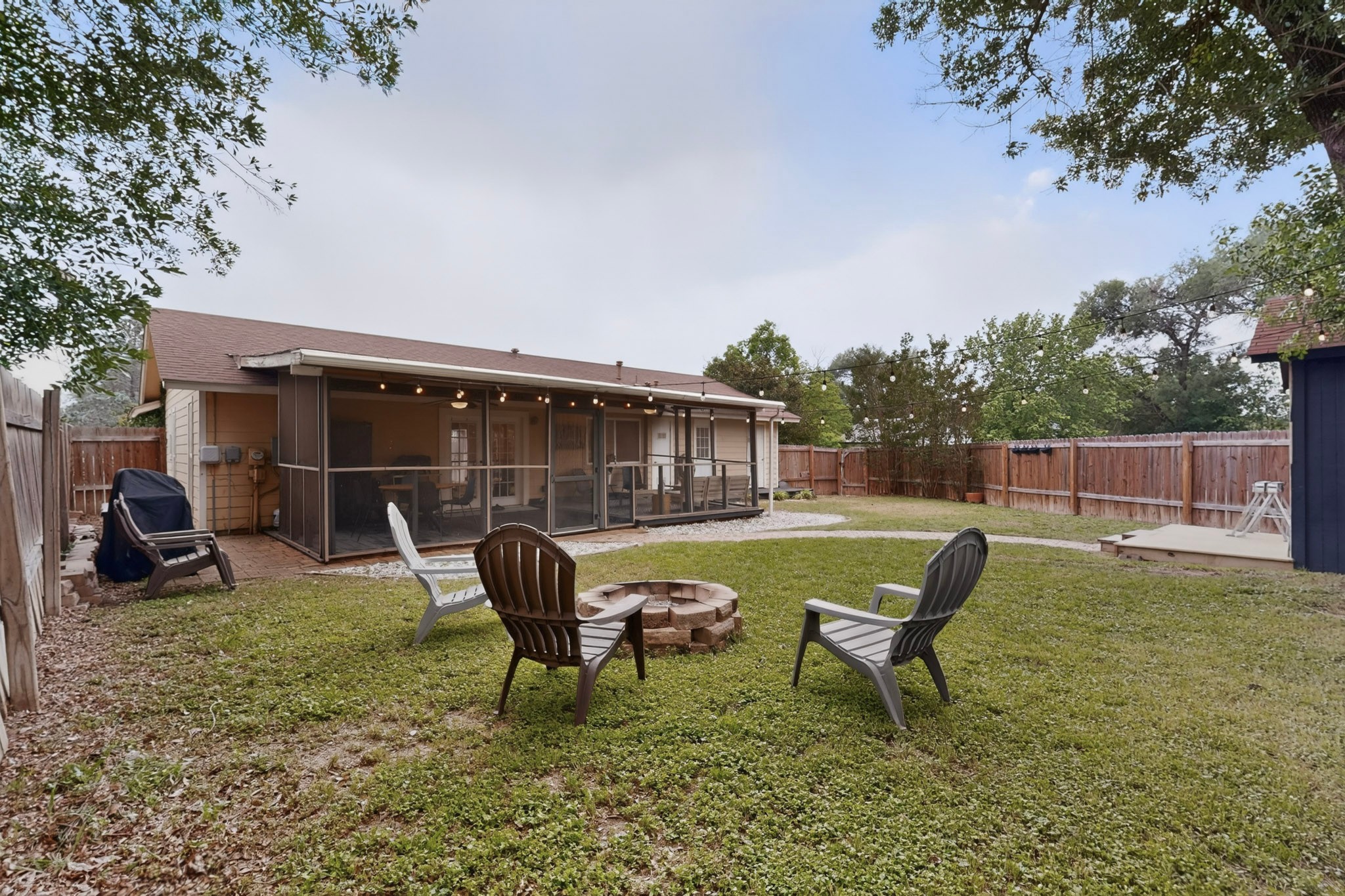 5541 Pine Place Austin, TX 78744 - Photo 33 of 33 Expansive backyard featuring a screened-in porch with string lighting, a stone fire pit, a wooden privacy fence, and a separate wooden deck